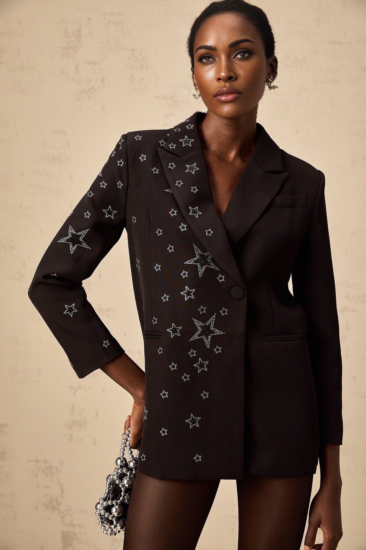 A black blazer featuring star appliques worn by a model standing against a plain background