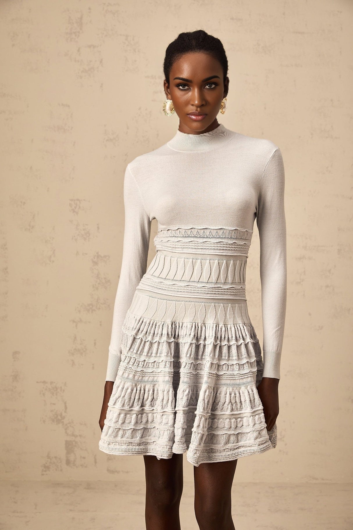 A grey mini dress with ruffled details and a ribbed knit texture featuring a fitted silhouette and short length