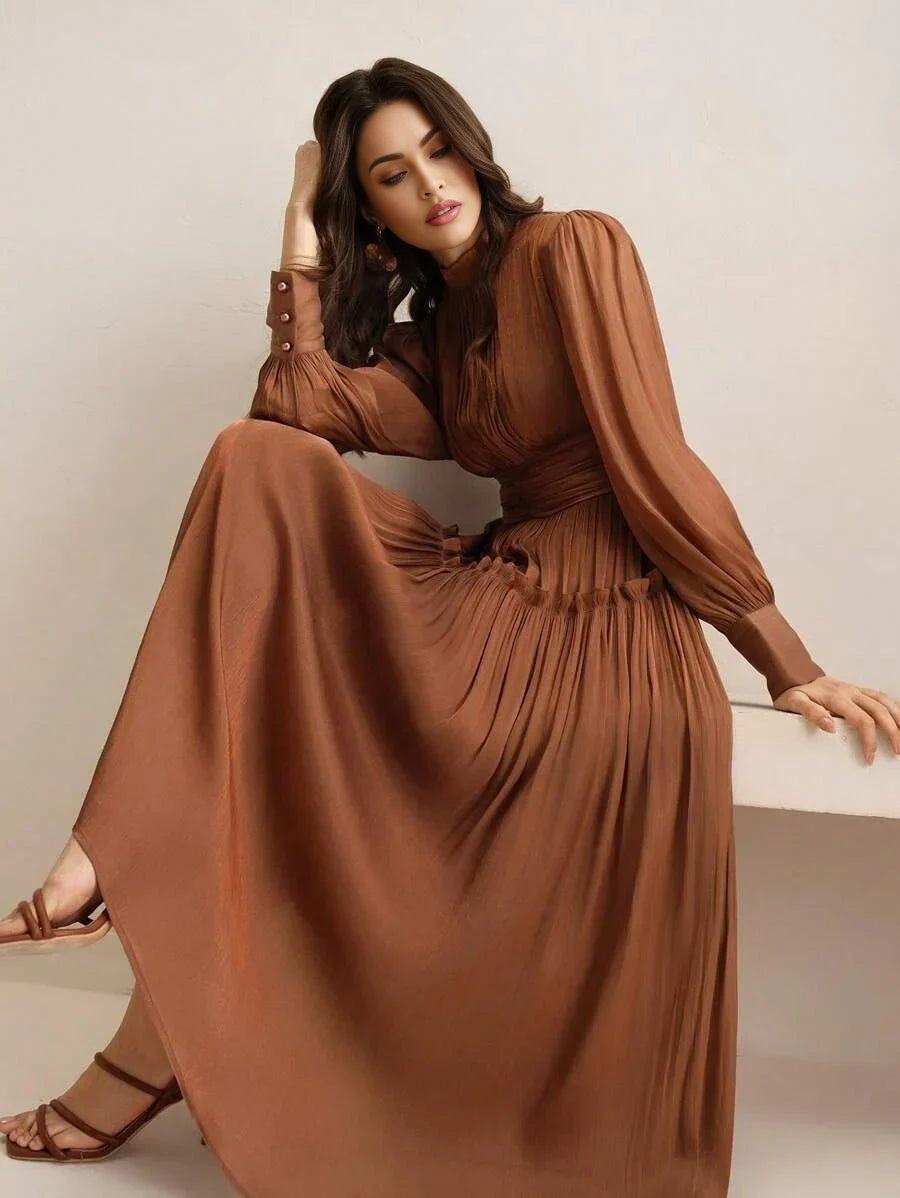 This graceful long-sleeved dress features a rich, earthy brown hue, accentuated by pleated detailing that enhances its flowy.