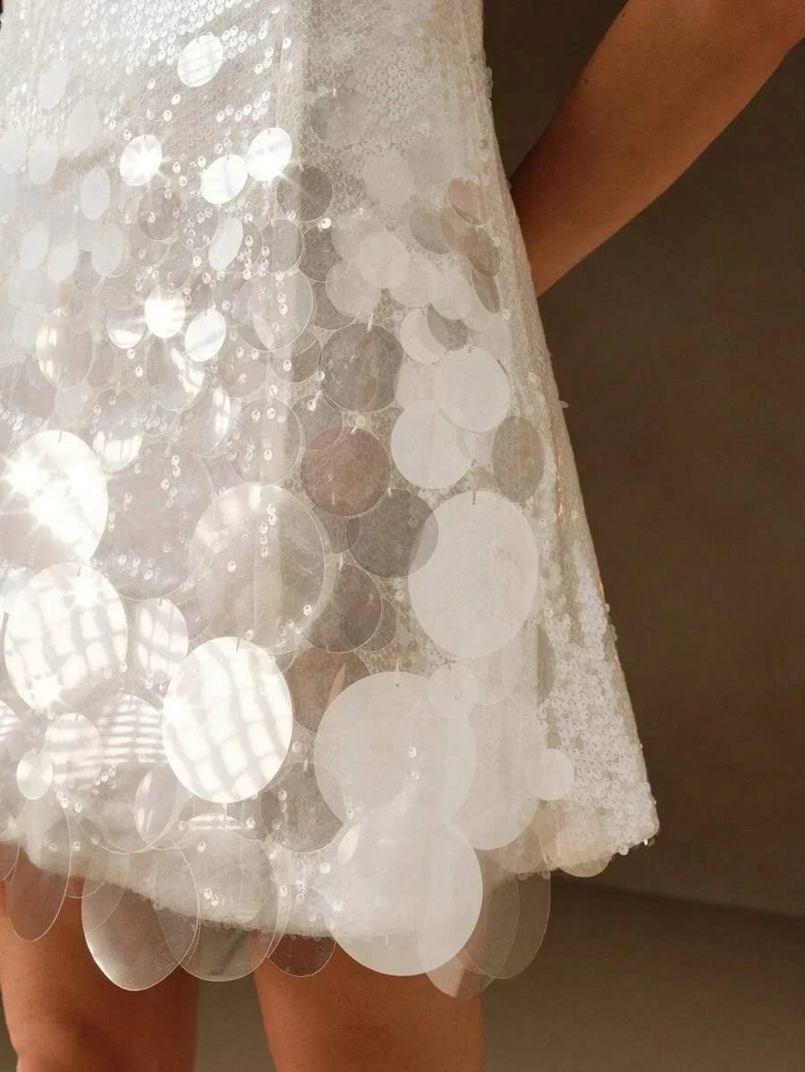 This enchanting white dress features a playful fit-and-flare silhouette adorned with shimmering sequins and large.