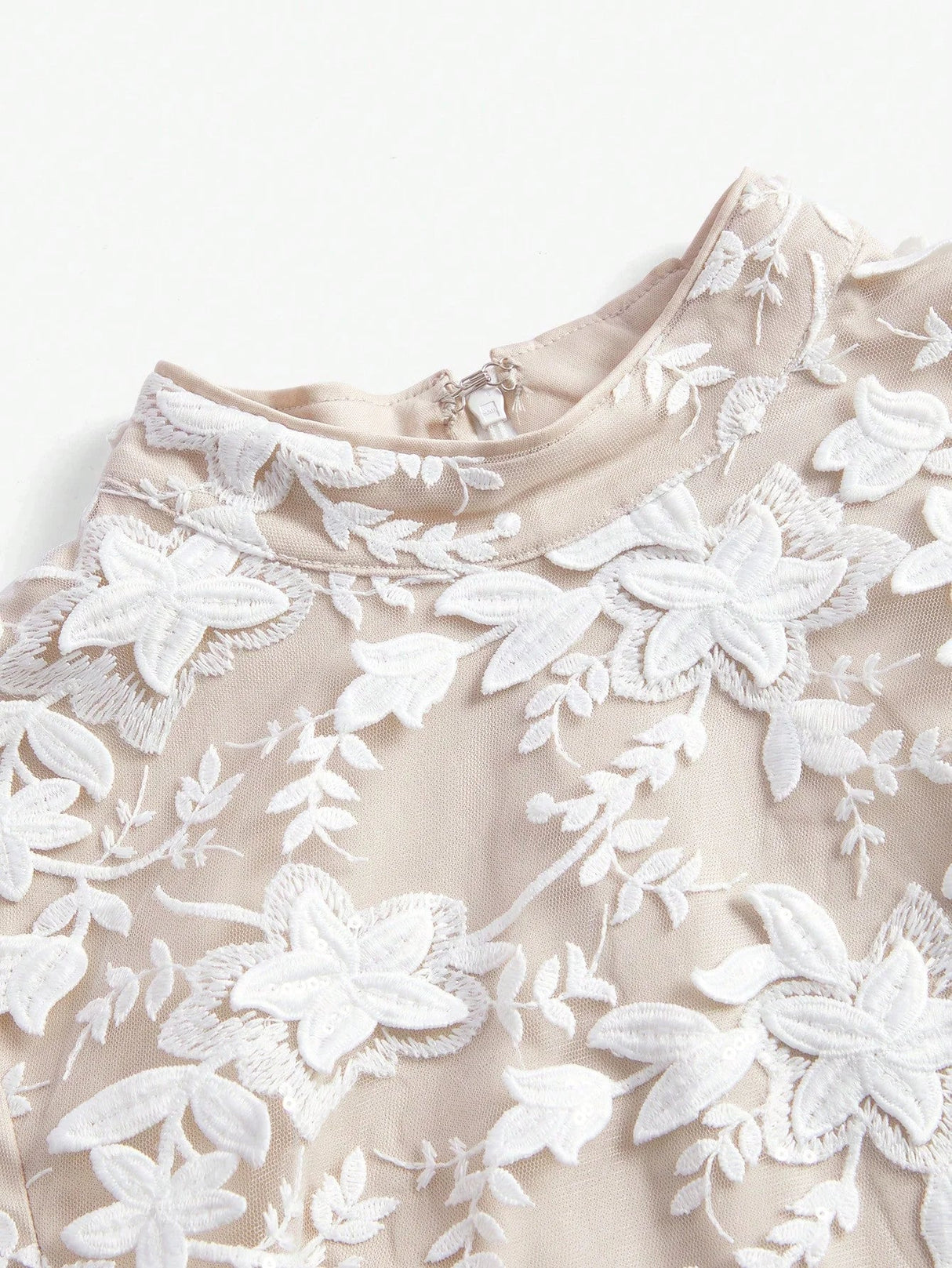 Elegant beige dress adorned with intricate white floral embroidery, featuring a refined high neckline and a soft, flowing.