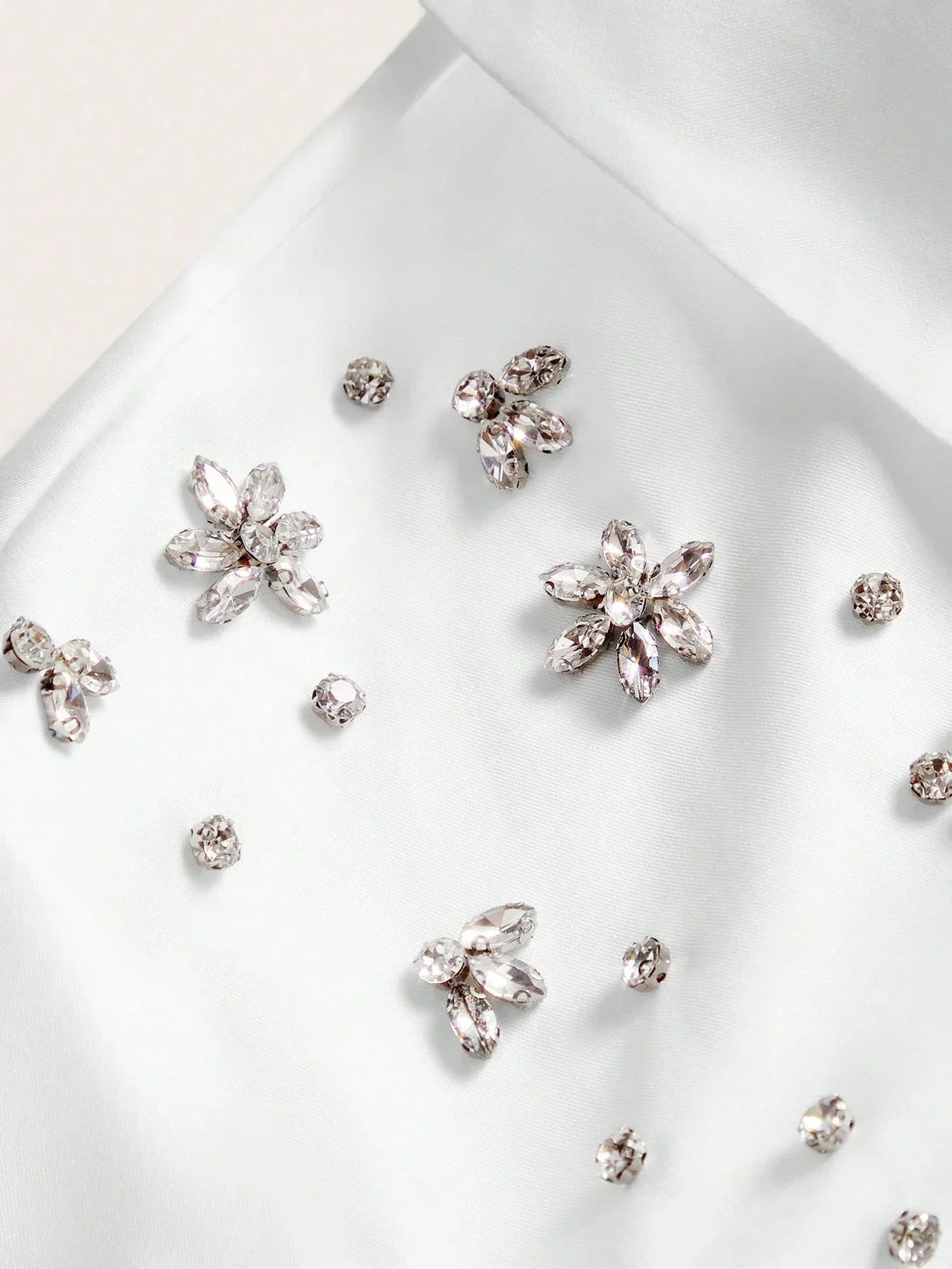 Delicate white satin fabric adorned with sparkling jewel embellishments in floral shapes creates a breathtakingly elegant.