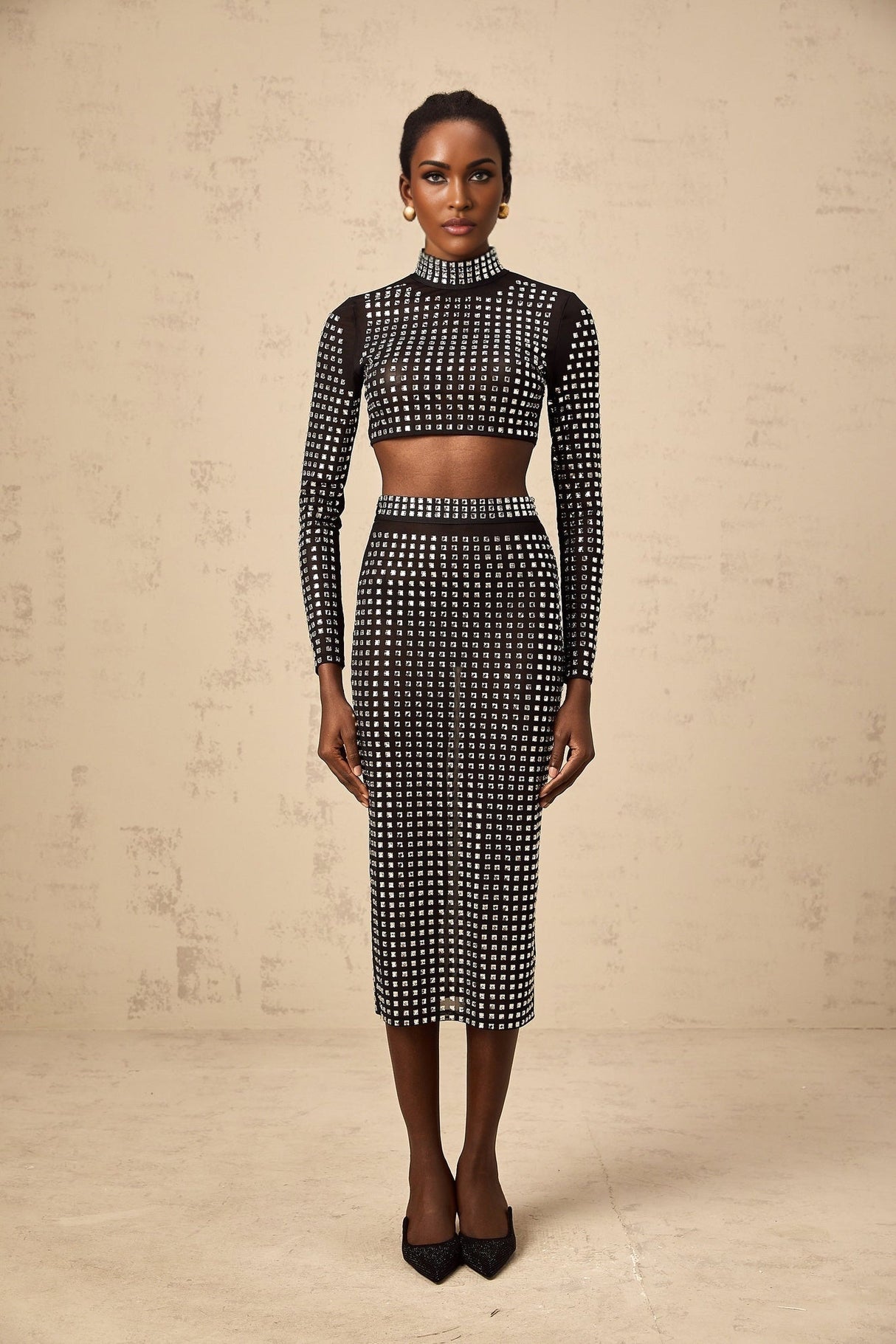 Woman wearing a black twopiece outfit consisting of a rhinestoneembellished mesh top and matching skirt