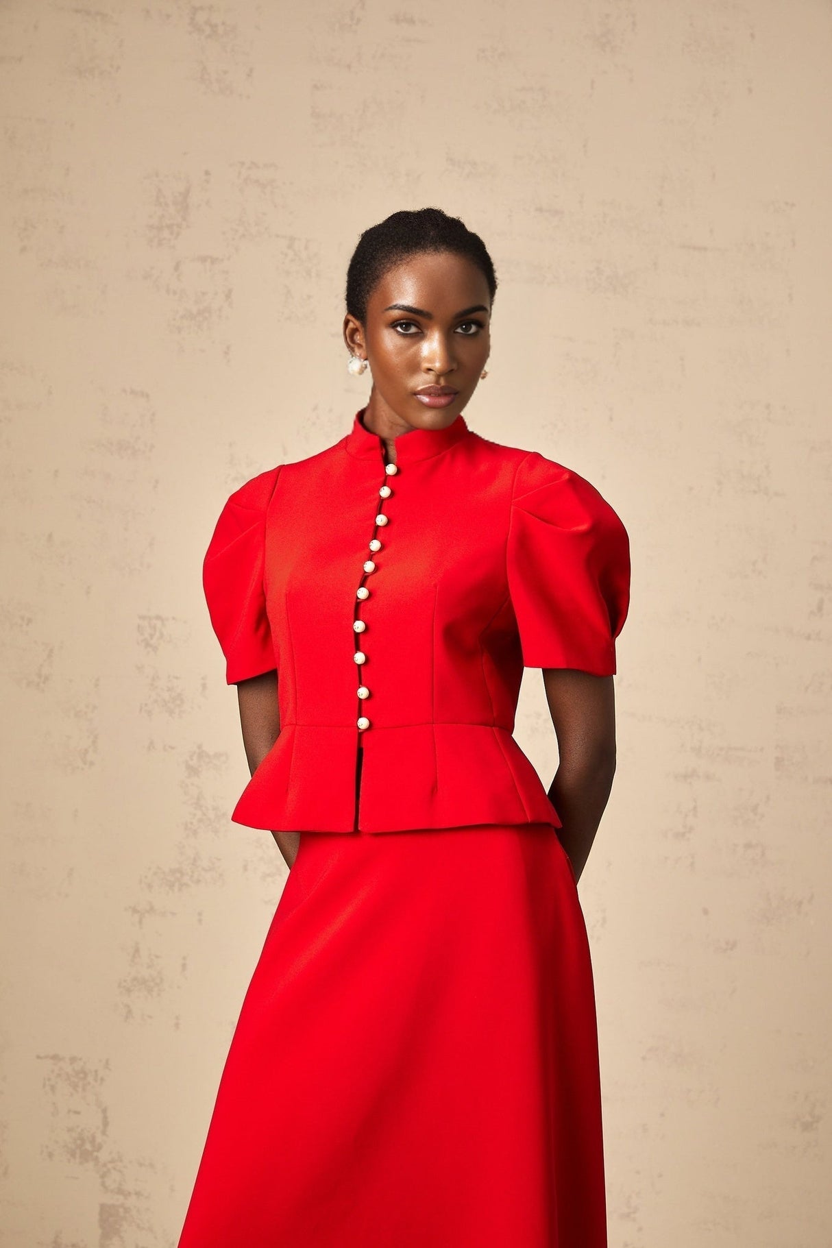 Woman wearing a red pleated blouse and matching skirt set named Colette