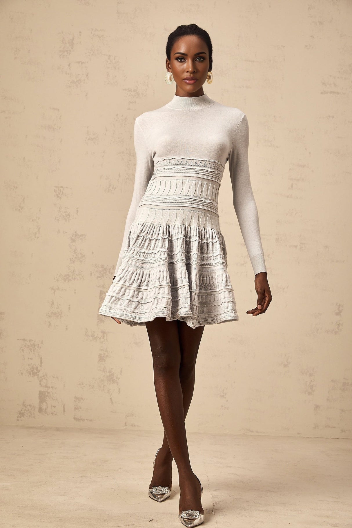 Woman wearing a short grey dress with ruffled details and ribbed texture standing against a plain background