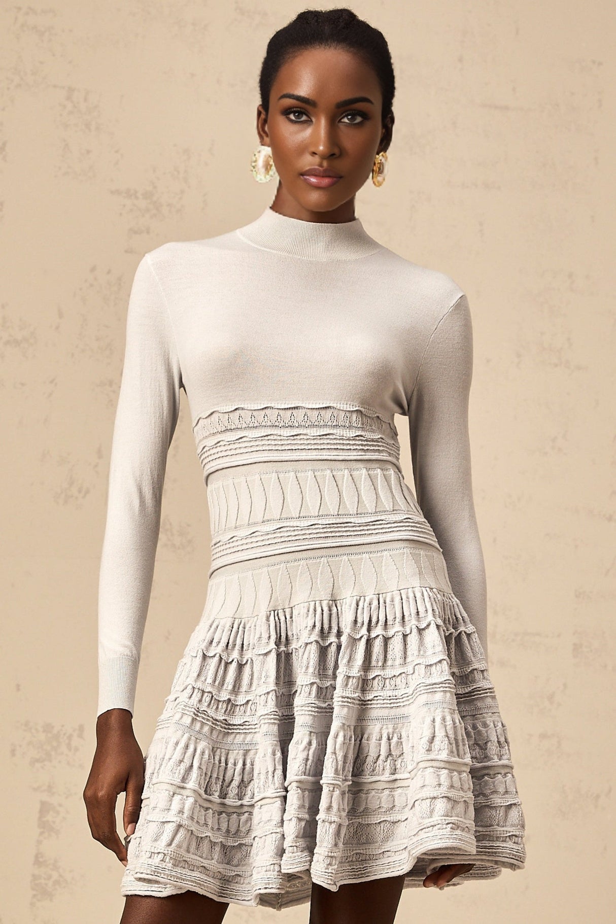 Woman wearing short grey ribbed knit dress with ruffled details and long sleeves