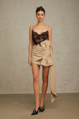A beige mini skirt with ruched detailing and a large bow accent at the waist
