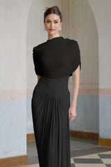 A black asymmetric maxi dress with pleated details and a flowing silhouette worn by a model standing against a plain background