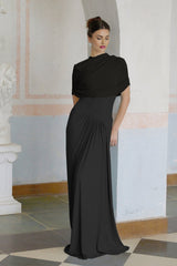 A black asymmetric maxi dress with pleats named Catherine worn by a model standing against a plain background