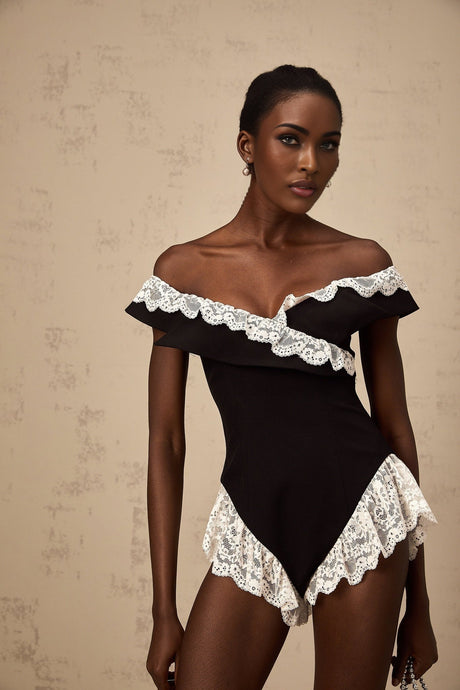 A black bodysuit with delicate lace trim details worn by a female model against a plain background