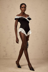 A black bodysuit with delicate lace trim worn by a model against a plain background