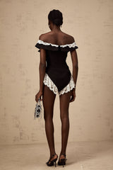 A black bodysuit with lace trim detailing worn by a model standing against a plain background