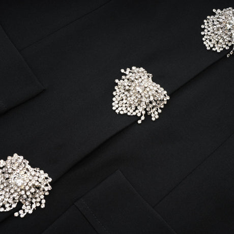 A black crystal embellished mini dress with a sleek design and shimmering texture worn by a model against a plain background