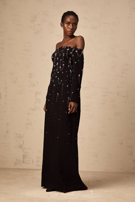 A black crystalembellished offshoulder maxi dress on a mannequin or model showcasing the elegant Gabrielle design with a flowing floorlength skirt