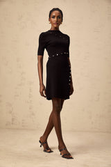 A black fineknit mini dress with decorative buttons named Wanda worn by a model against a plain background