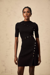 A black fineknit mini dress with decorative buttons worn by a model named Wanda