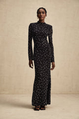 A black floor length maxi dress with sheer elements and decorative embellishments worn by a model