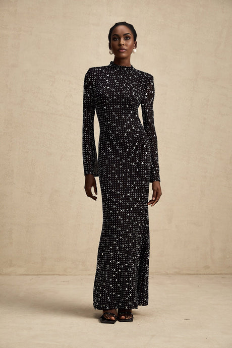 A black floor length maxi dress with sheer elements and decorative embellishments worn by a model