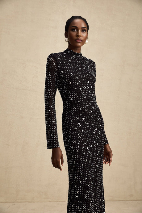 A black floor length maxi dress with sheer elements and decorative embellishments worn by a model