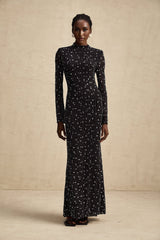 A black floor length maxi dress with sheer elements and embellished details modeled on a woman