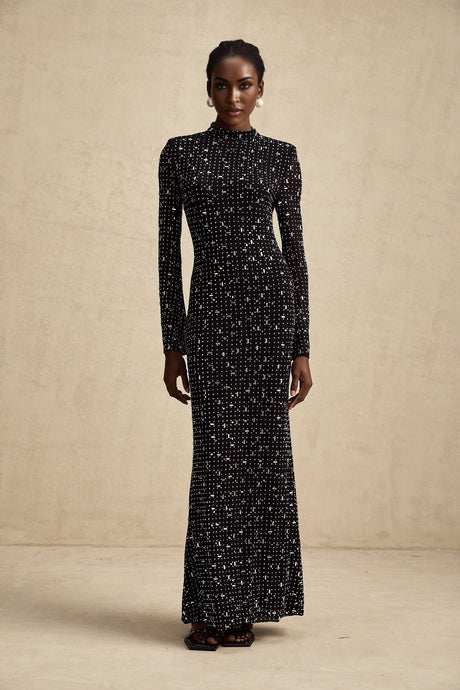 A black floor length maxi dress with sheer elements and embellished details modeled on a woman