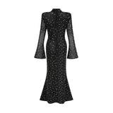 A black floor length maxi dress with sheer elements and embellished details worn by a model standing against a plain background
