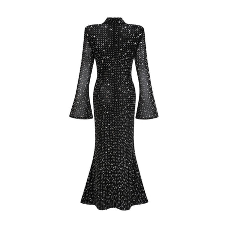 A black floor length maxi dress with sheer elements and embellished details worn by a model standing against a plain background