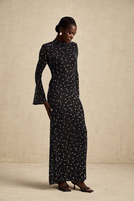 A black floor length maxi dress with sheer elements and embellishments worn by a model
