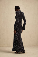 A black floor length maxi dress with sheer fabric and embellished details worn by a model standing against a plain background
