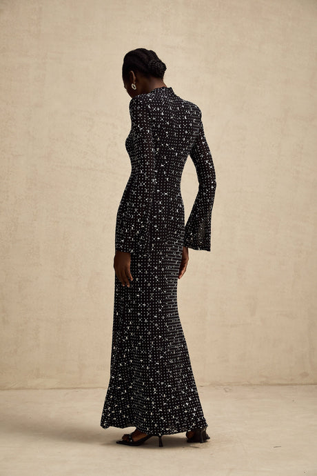 A black floor length maxi dress with sheer fabric and embellished details worn by a model standing against a plain background