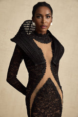A black floorlength fishtail dress with structured detailing and a split feature worn by a model standing against a plain background