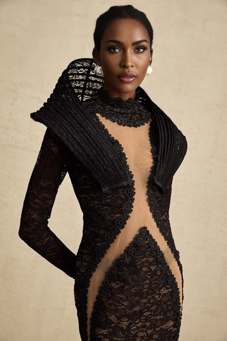 A black floorlength fishtail dress with structured detailing and a split feature worn by a model standing against a plain background