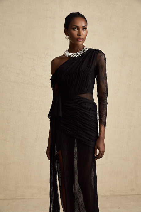 A black floorlength maxi dress with a single shoulder strap and a cut out detail on one side worn by a model against a plain background