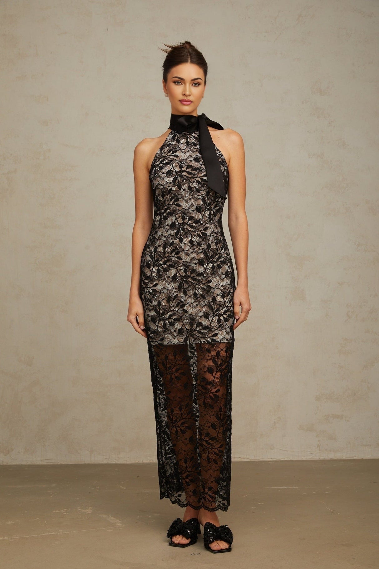 A black floral lace maxi dress with a halter neckline named Coralie featuring a long flowing skirt and delicate lace pattern throughout