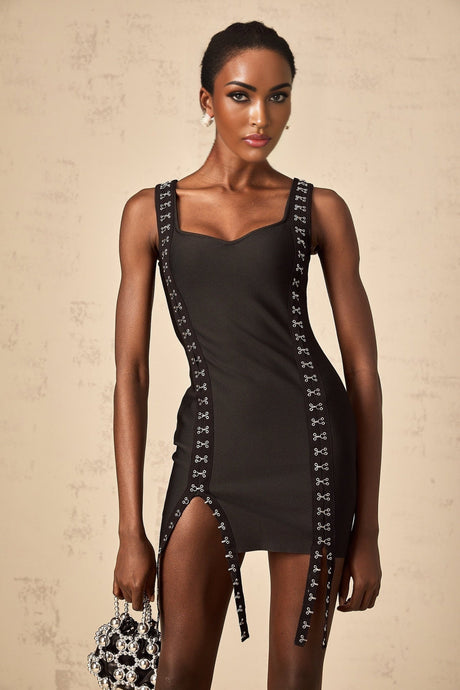 A black formfitting mini dress with a bandage style design and hookandeye closures worn by a model against a plain background