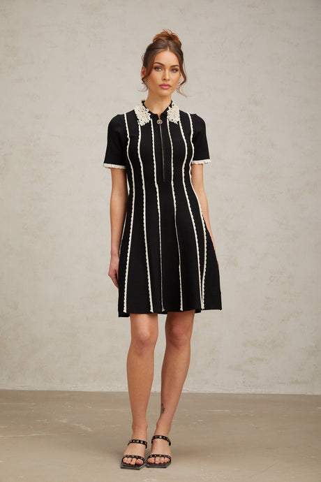 A black knit mini dress with vertical white stripes and ruffle trim details on a female model