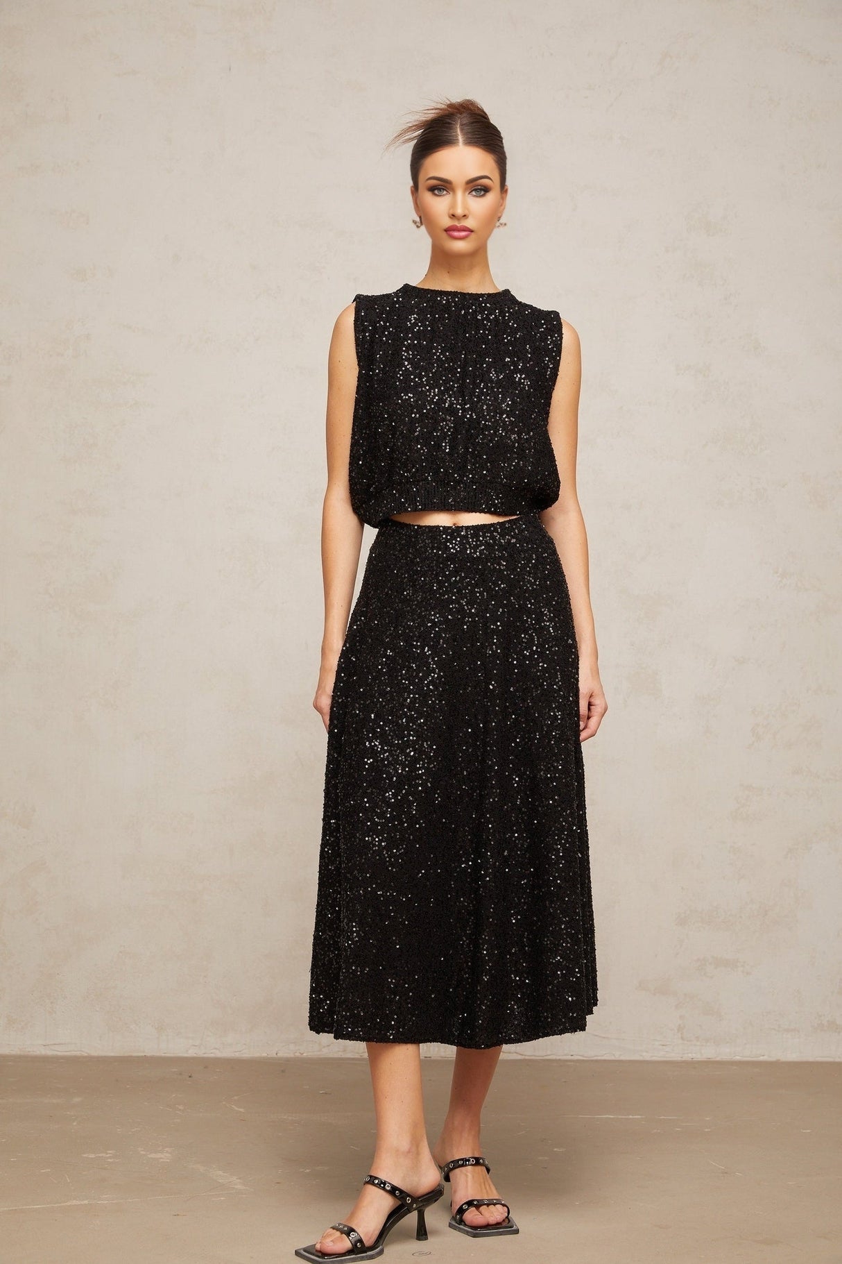 A black knit vest and skirt set adorned with sequins creating a shimmering effect Both pieces feature a matching sequined pattern The vest is sleeveless and the skirt appears to be knee length Together they form a coordinated and elegant outfit