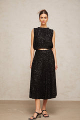 A black knit vest and skirt set adorned with sequins creating a shimmering effect Both pieces feature a matching sequined pattern The vest is sleeveless and the skirt appears to be knee length Together they form a coordinated and elegant outfit