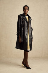 A black leather coat with double breasted front and belt at the waist worn by a model named Camille