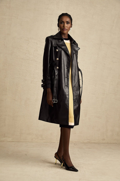 A black leather coat with double breasted front and belt at the waist worn by a model named Camille