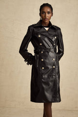 A black leather coat with doublebreasted front closure and a belt cinching the waist worn by a model against a plain background
