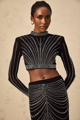 A black matching set consisting of a rhinestoneembellished mesh top and skirt worn by a model against a plain background