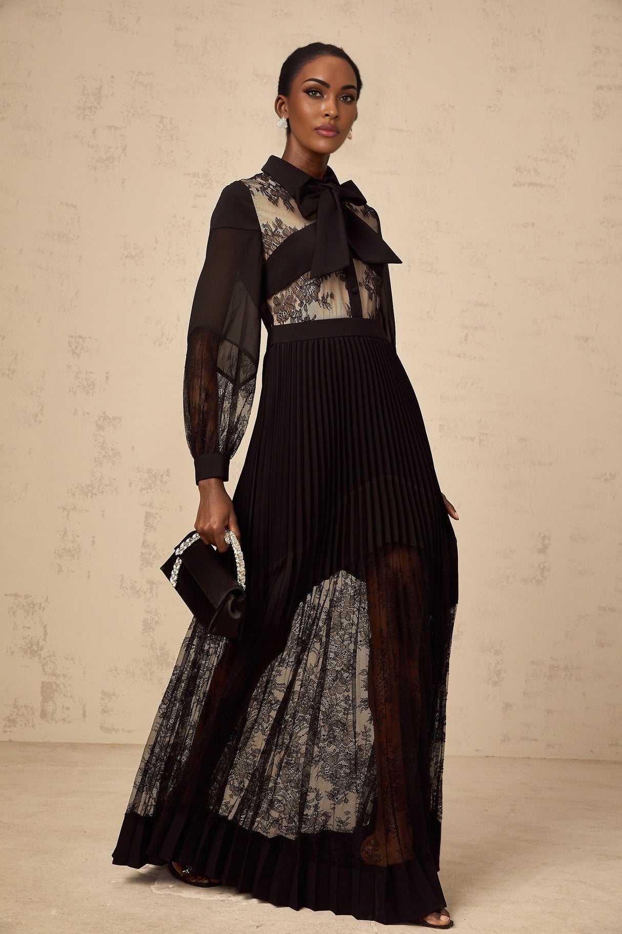 A black maxi dress with floral lace panels and pleated details named Segolene