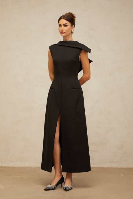 A black midi dress with an open back and deconstructed design worn by a model standing against a plain background
