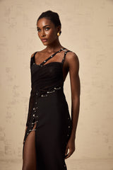 A black midi dress with asymmetric design and cut out details worn by a model against a plain background