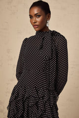 A black midi dress with white polka dots featuring ruffled details and a feminine silhouette named Coraline