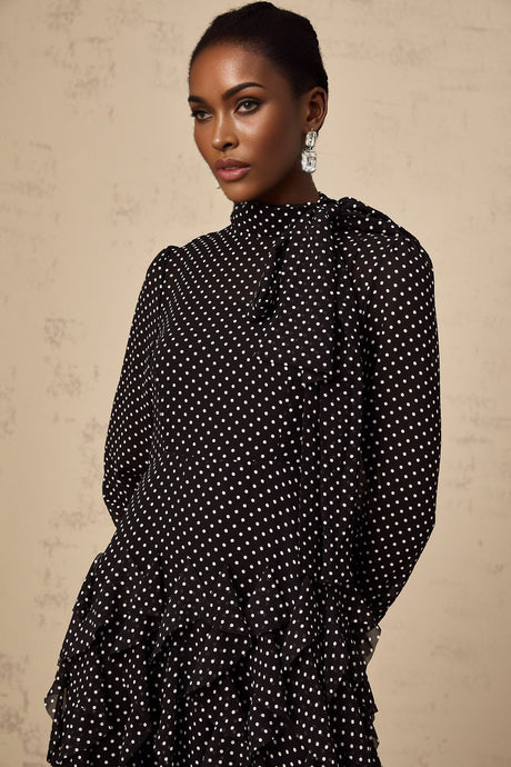 A black midi dress with white polka dots featuring ruffled details and a feminine silhouette named Coraline
