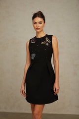 A black mini dress adorned with sequins featuring a butterfly design worn by a model against a plain background