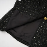 A black mini dress featuring a tweed fabric with sequin panels named Audrey combining classic and glamorous elements in a short silhouette