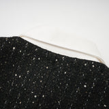 A black mini dress with a tweed fabric base featuring sequin panels on the bodice creating a sparkling contrast the dress has short sleeves and a fitted silhouette inspired by classic Audrey Hepburn style